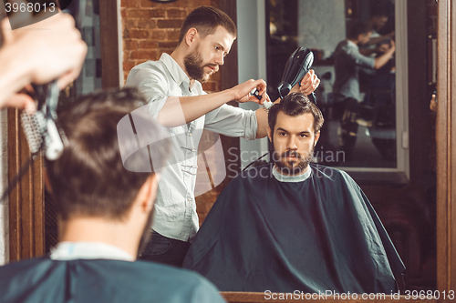 Image of Young handsome barber making haircut of attractive man in barbershop