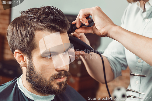 Image of The hands of young barber making haircut  attractive man in barbershop