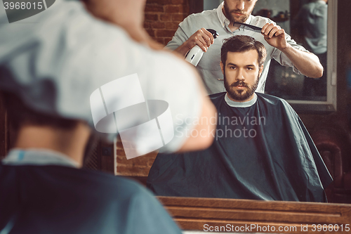 Image of Young handsome barber making haircut of attractive man in barbershop