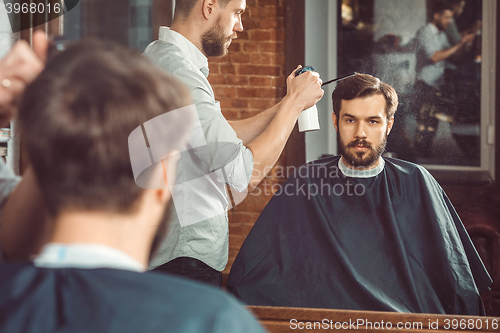 Image of Young handsome barber making haircut of attractive man in barbershop