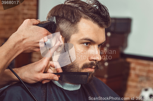 Image of The hands of young barber making haircut to attractive man in barbershop