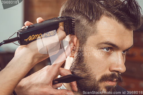 Image of The hands of young barber making haircut to attractive man in barbershop