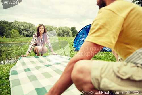 Image of happy couple laying picnic blanket at campsite