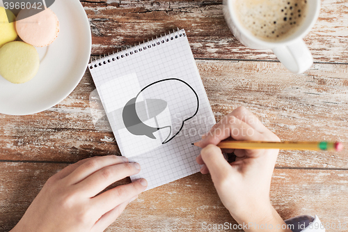 Image of close up of hands drawing text bubble to notebook