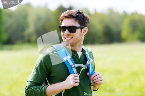 Image of happy young man with backpack hiking outdoors