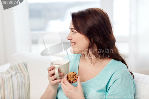 Image of happy plus size woman with cup and cookie at home