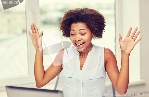 Image of happy african woman with laptop at office