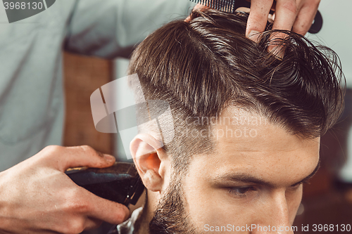 Image of The hands of young barber making haircut to attractive man in barbershop