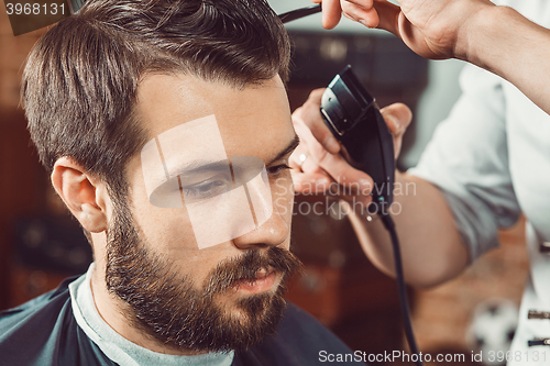 Image of The hands of young barber making haircut  attractive man in barbershop