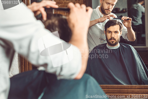 Image of Young handsome barber making haircut of attractive man in barbershop