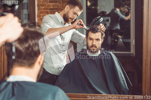 Image of Young handsome barber making haircut of attractive man in barbershop