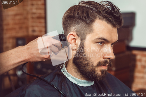 Image of The hands of young barber making haircut to attractive man in barbershop