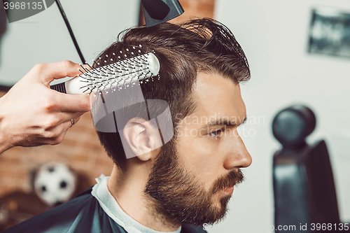 Image of The hands of young barber making haircut attractive man in barbershop