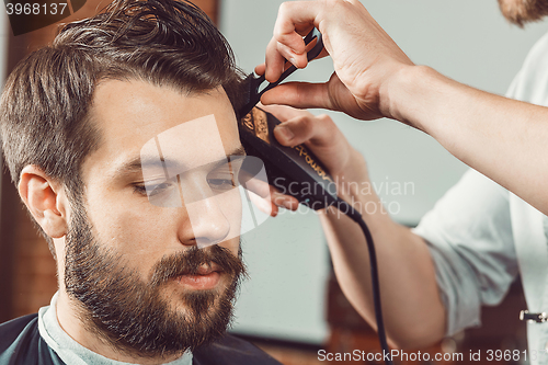 Image of The hands of young barber making haircut  attractive man in barbershop