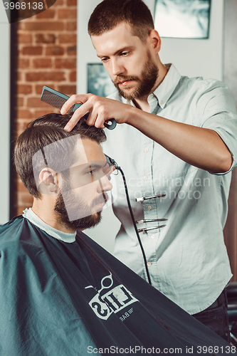 Image of Young handsome barber making haircut of attractive man in barbershop