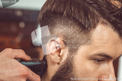 Image of The hands of young barber making haircut to attractive man in barbershop