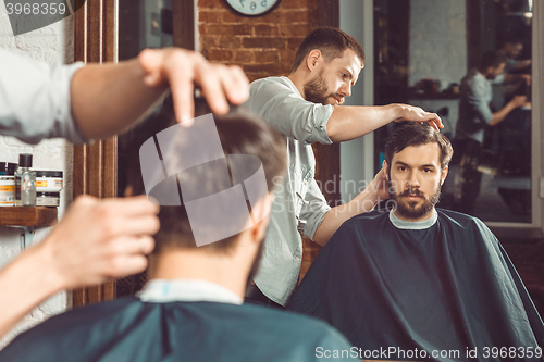 Image of Young handsome barber making haircut of attractive man in barbershop