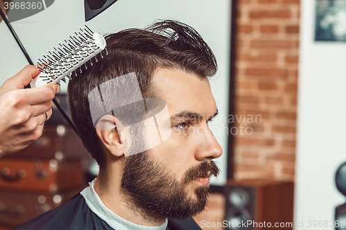 Image of The hands of young barber making haircut attractive man in barbershop