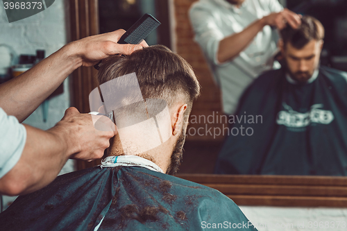 Image of The hands of young barber making haircut to attractive man in barbershop