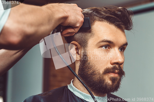 Image of The hands of young barber making haircut to attractive man in barbershop