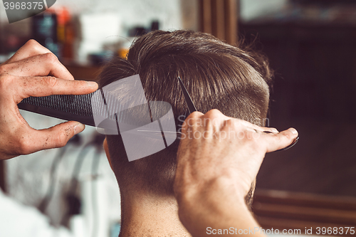 Image of The hands of young barber making haircut to attractive man in barbershop