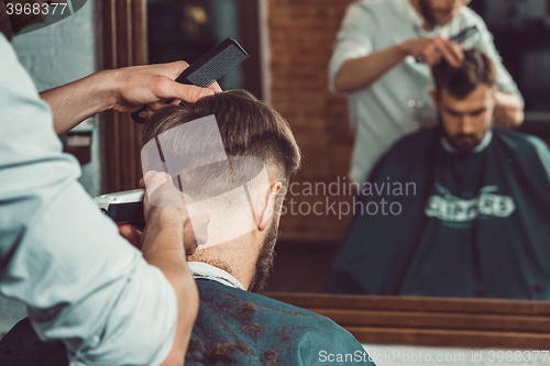 Image of The hands of young barber making haircut to attractive man in barbershop