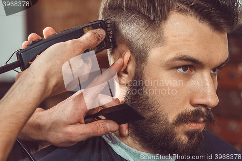 Image of The hands of young barber making haircut to attractive man in barbershop