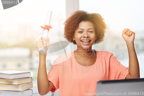 Image of happy african woman with laptop, books and diploma
