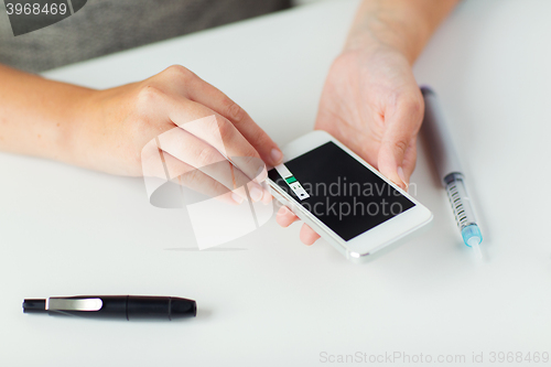 Image of close up of woman with smartphone doing blood test