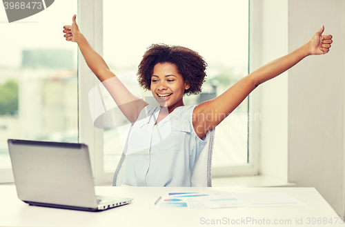 Image of happy african woman with laptop at office