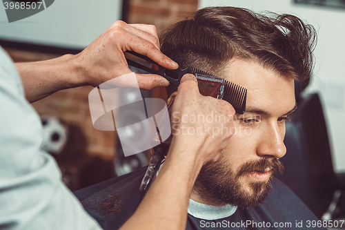 Image of The hands of young barber making haircut to attractive man in barbershop