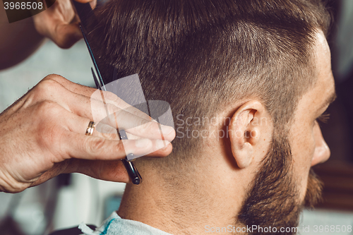 Image of The hands of young barber making haircut to attractive man in barbershop