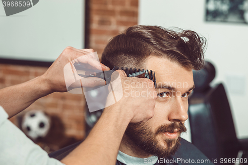 Image of The hands of young barber making haircut to attractive man in barbershop