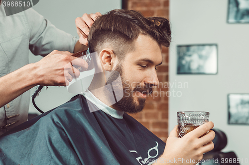 Image of The hands of young barber making haircut to attractive man in barbershop