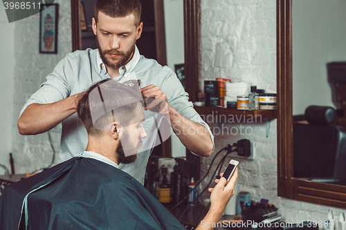 Image of Young handsome barber making haircut of attractive man in barbershop