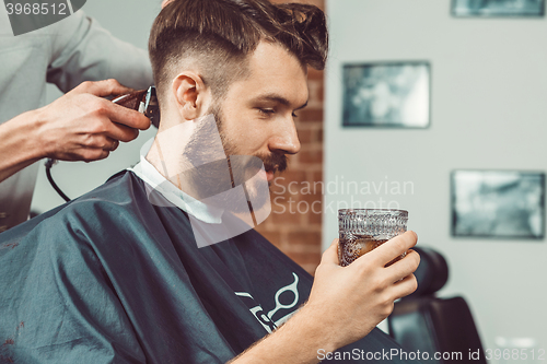 Image of The hands of young barber making haircut to attractive man in barbershop