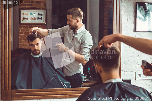 Image of Young handsome barber making haircut of attractive man in barbershop