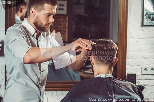 Image of Young handsome barber making haircut of attractive man in barbershop