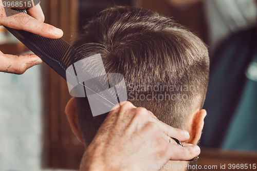 Image of The hands of young barber making haircut to attractive man in barbershop