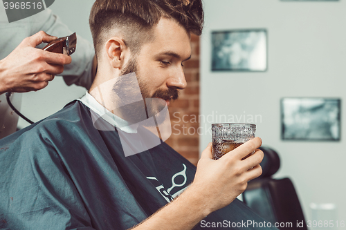 Image of The hands of young barber making haircut to attractive man in barbershop