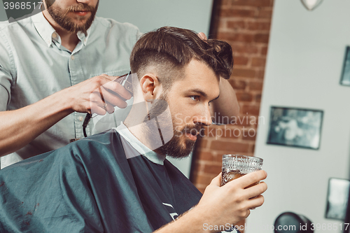 Image of Young handsome barber making haircut of attractive man in barbershop