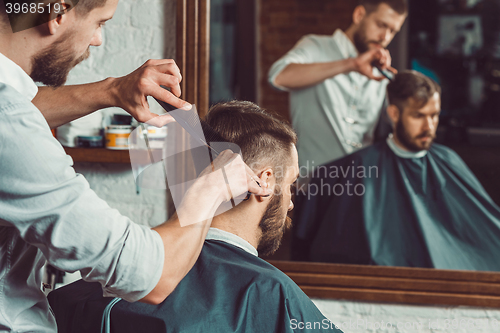 Image of Young handsome barber making haircut of attractive man in barbershop