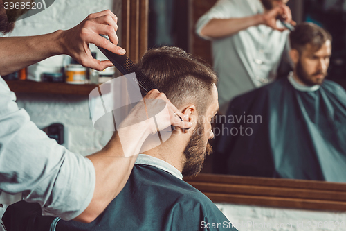 Image of The hands of young barber making haircut to attractive man in barbershop