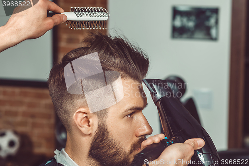 Image of The hands of young barber making haircut to attractive man in barbershop