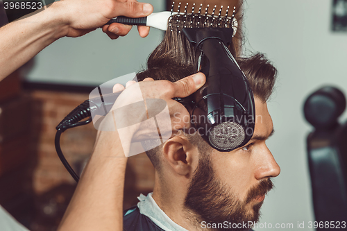 Image of The hands of young barber making haircut to attractive man in barbershop