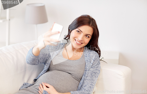 Image of pregnant woman taking smartphone selfie at home