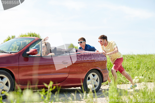 Image of happy friends pushing broken cabriolet car