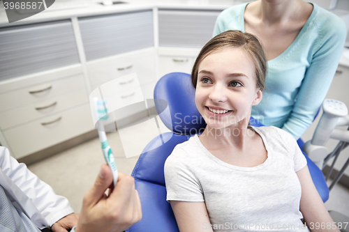 Image of happy dentist showing toothbrush to patient girl