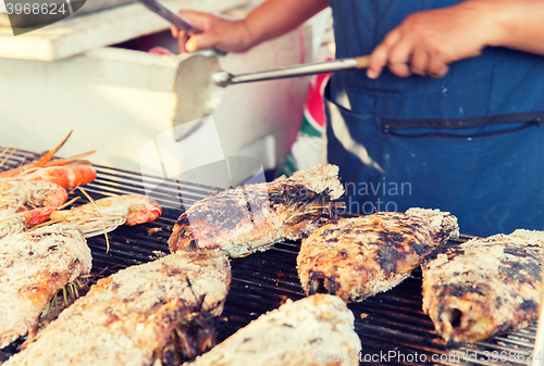 Image of close up of cook hands grilling fish on street