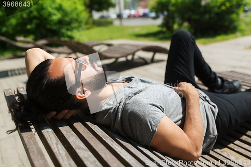 Image of happy man lying on street bench or sun bed 